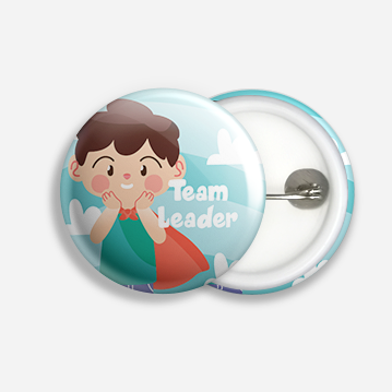 A button badge with a cartoon image of a small child wearing a cape, and labelled “Team Leader”.