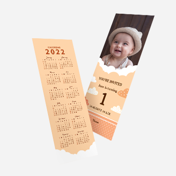 A salmon pink bookmark with a calendar for 2022 on one side, and an image of a smiling baby on the other side. The bookmark also appears to serve as an invitation to the baby’s first birthday.