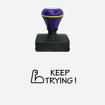 A rubber stamp that says “Keep Trying” with a blue handle.